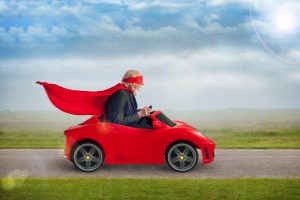 senior superhero with mask and cape driving a toy sports car